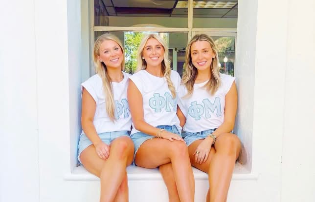 3 sisters sitting on window ceil smiling at camrea wearing matching clothes