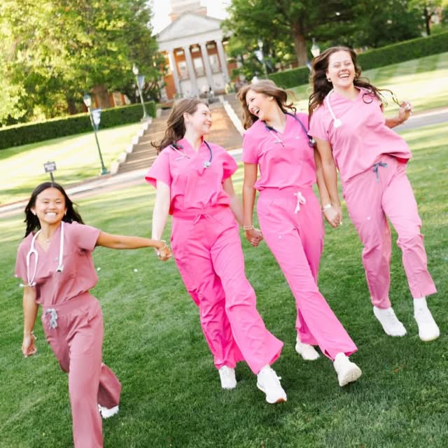 4 sisters in nurse pink scrubs walking toward the camera smiling on campus