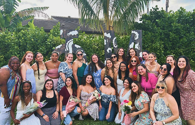 group of sisters posing for a photo holding flowers outside near palm trees